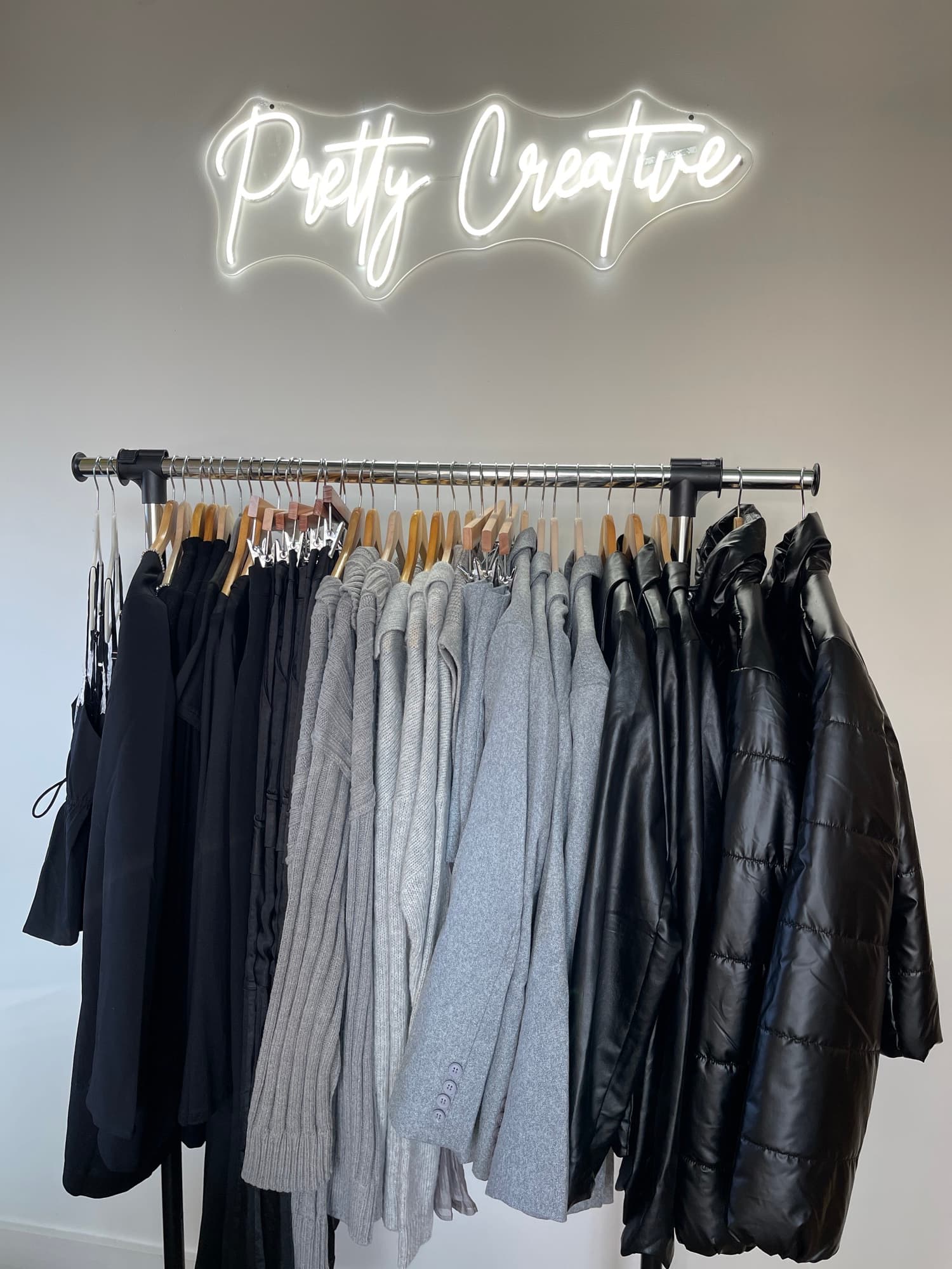 A curated rail of knits and leather beneath the glowing Pretty Creative neon script