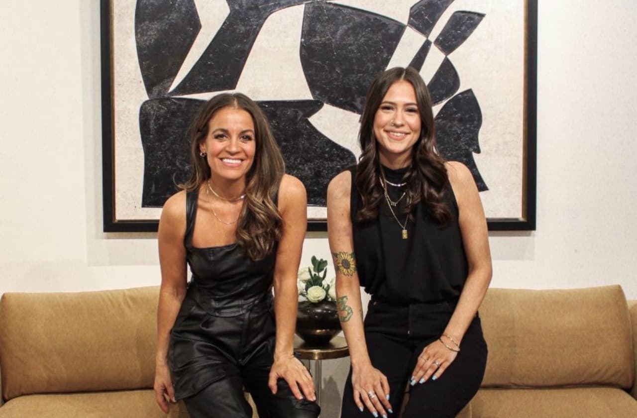 Two women seated together beneath a large abstract artwork